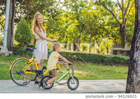 Happy family is riding bikes outdoors and smiling. Mom on a bike and son on a balancebike 94526023