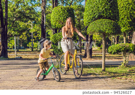 Happy family is riding bikes outdoors and smiling. Mom on a bike and son on a balancebike 94526027