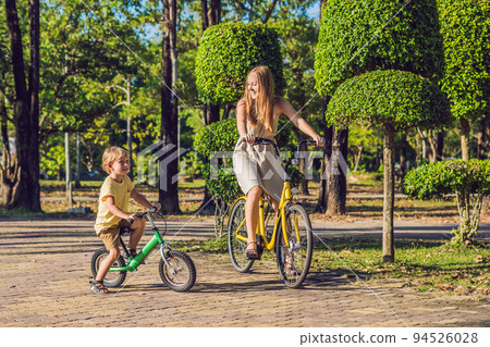 Happy family is riding bikes outdoors and smiling. Mom on a bike and son on a balancebike 94526028