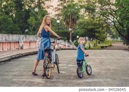 Happy family is riding bikes outdoors and smiling. Mom on a bike and son on a balancebike 94526045