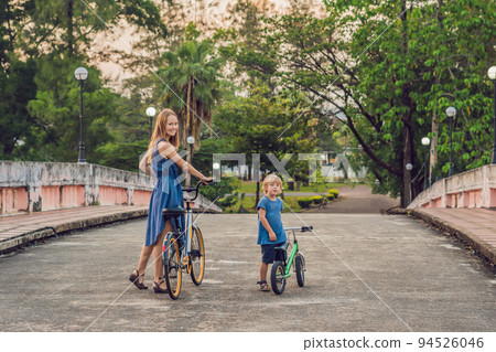 Happy family is riding bikes outdoors and smiling. Mom on a bike and son on a balancebike 94526046