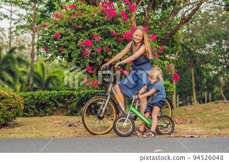 Happy family is riding bikes outdoors and smiling. Mom on a bike and son on a balancebike 94526048