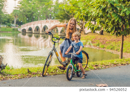 Happy family is riding bikes outdoors and smiling. Mom on a bike and son on a balancebike 94526052
