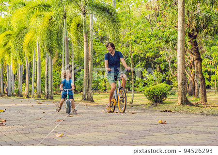 Happy family is riding bikes outdoors and smiling. Father on a bike and son on a balancebike 94526293