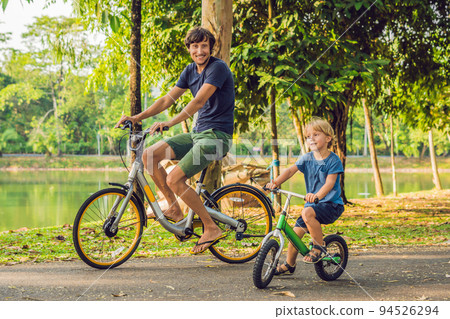Happy family is riding bikes outdoors and smiling. Father on a bike and son on a balancebike 94526294