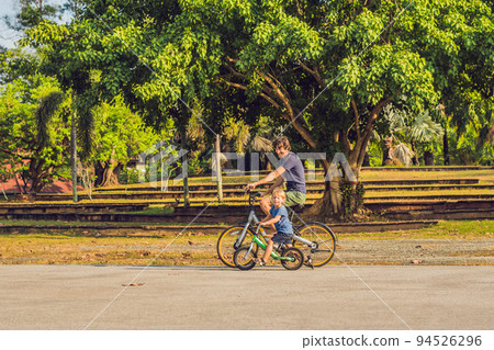 Happy family is riding bikes outdoors and smiling. Father on a bike and son on a balancebike 94526296