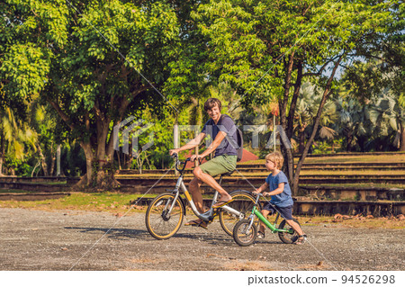 Happy family is riding bikes outdoors and smiling. Father on a bike and son on a balancebike Happy family is riding bikes outdoors and smiling. Father on a bike and son on a balancebike 94526298