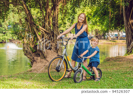 Happy family is riding bikes outdoors and smiling. Mom on a bike and son on a balancebike 94526307