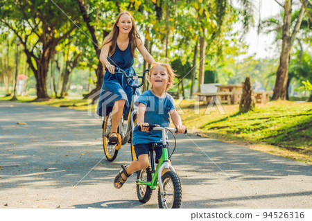 Happy family is riding bikes outdoors and smiling. Mom on a bike and son on a balancebike 94526316