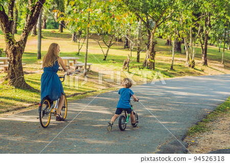 Happy family is riding bikes outdoors and smiling. Mom on a bike and son on a balancebike 94526318