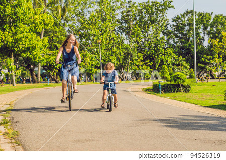 Happy family is riding bikes outdoors and smiling. Mom on a bike and son on a balancebike 94526319