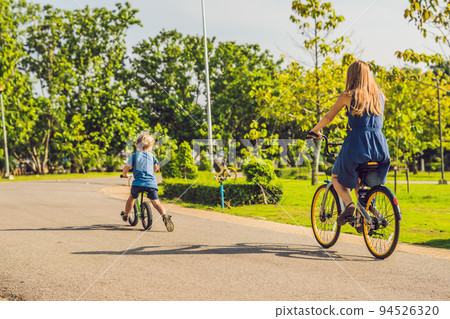 Happy family is riding bikes outdoors and smiling. Mom on a bike and son on a balancebike 94526320