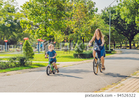 Happy family is riding bikes outdoors and smiling. Mom on a bike and son on a balancebike 94526322