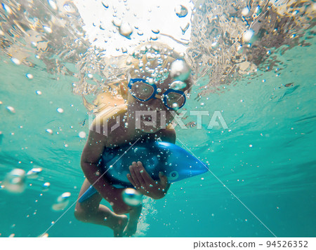 A child boy is swimming underwater in a pool, smiling and holding breath, with swimming glasses A child boy is swimming underwater in a pool, smiling and holding breath, with swimming glasses 94526352