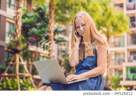 Young female freelancer sitting near the pool with her laptop in the hotel browsing in her smartphone. Busy at holidays. Distant work concept. Copy space for your text 94526812