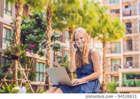 Young female freelancer sitting near the pool with her laptop in the hotel browsing in her smartphone. Busy at holidays. Distant work concept. Copy space for your text 94526813