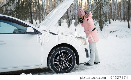 Young Woman Calling for Help or Assistance while Standing by the Open Hood of her Car in Winter Day Young Woman Calling for Help or Assistance while Standing by the Open Hood of her Car in Winter Day 94527574