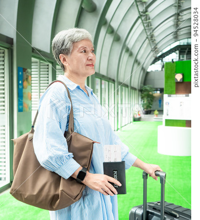 Portrait of senior adult elderly asian woman 60s smiling standing with suitcase luggage bag and holding passport with ticket for travel concept. 94528034