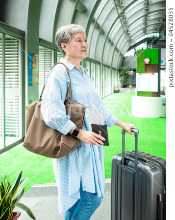 Portrait of senior adult elderly asian woman 60s smiling standing with suitcase luggage bag and holding passport with ticket for travel concept. 94528035