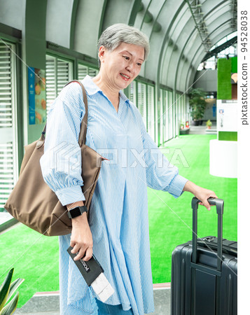 Portrait of senior adult elderly asian woman 60s smiling standing with suitcase luggage bag and holding passport with ticket for travel concept. 94528038