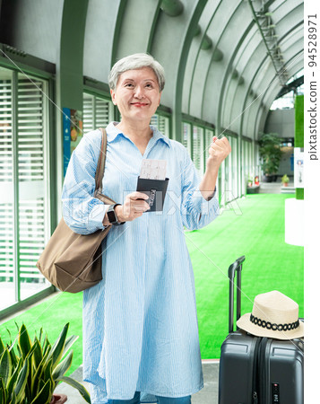 60多歲的亞洲熟年婦女微笑著站著,身旁有手提箱行李袋和手持登機證與護照,適用於covid19疫情後旅 60多歲的亞洲熟年婦女微笑著站著,身旁有手提箱行李袋和手持登機證與護照,適用於covid19疫情後旅 94528971