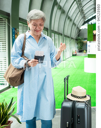 60多歲的亞洲熟年婦女微笑著站著,身旁有手提箱行李袋和手持登機證與護照,適用於covid19疫情後旅 60多歲的亞洲熟年婦女微笑著站著,身旁有手提箱行李袋和手持登機證與護照,適用於covid19疫情後旅 94528980