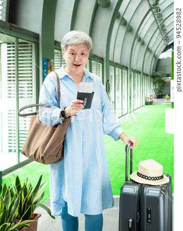 60多歲的亞洲熟年婦女微笑著站著,身旁有手提箱行李袋和手持登機證與護照,適用於covid19疫情後旅 60多歲的亞洲熟年婦女微笑著站著,身旁有手提箱行李袋和手持登機證與護照,適用於covid19疫情後旅 94528982