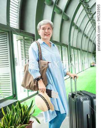 60多歲的亞洲熟年婦女微笑著站著,身旁有手提箱行李袋和手持登機證與護照,適用於covid19疫情後旅 60多歲的亞洲熟年婦女微笑著站著,身旁有手提箱行李袋和手持登機證與護照,適用於covid19疫情後旅 94528995