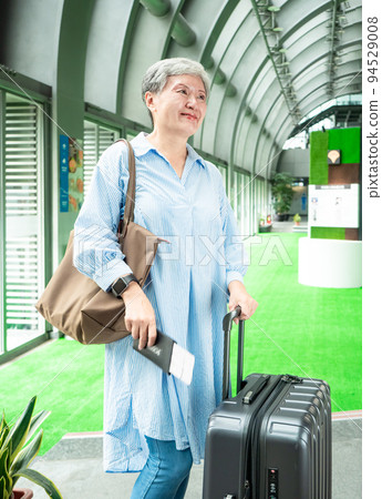 60多歲的亞洲熟年婦女微笑著站著,身旁有手提箱行李袋和手持登機證與護照,適用於covid19疫情後旅 60多歲的亞洲熟年婦女微笑著站著,身旁有手提箱行李袋和手持登機證與護照,適用於covid19疫情後旅 94529008