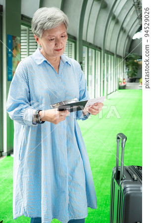 60多歲的亞洲熟年婦女微笑著站著,身旁有手提箱行李袋和手持登機證與護照,適用於covid19疫情後旅 60多歲的亞洲熟年婦女微笑著站著,身旁有手提箱行李袋和手持登機證與護照,適用於covid19疫情後旅 94529026