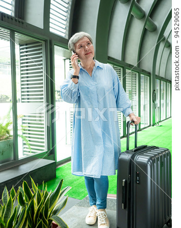 60多歲的亞洲熟年婦女微笑著站在身旁有手提箱行李袋和使用智能手機,適用於covid19疫情後旅行的概 60多歲的亞洲熟年婦女微笑著站在身旁有手提箱行李袋和使用智能手機,適用於covid19疫情後旅行的概 94529065