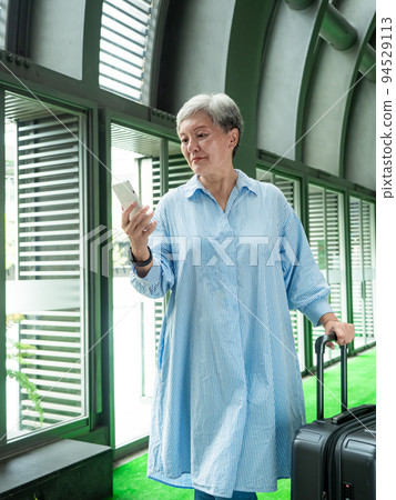60多歲的亞洲熟年婦女微笑著站在身旁有手提箱行李袋和使用智能手機,適用於covid19疫情後旅行的概 60多歲的亞洲熟年婦女微笑著站在身旁有手提箱行李袋和使用智能手機,適用於covid19疫情後旅行的概 94529113