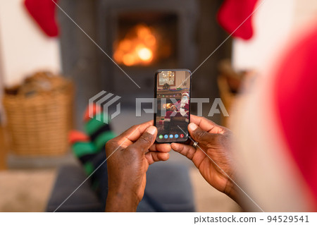 African american man in santa hat on christmas video call on smartphone with santa claus African american man in santa hat on christmas video call on smartphone with santa claus 94529541