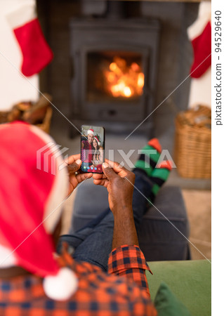 African american man in santa hat on christmas video call on smartphone with caucasian couple 94529640