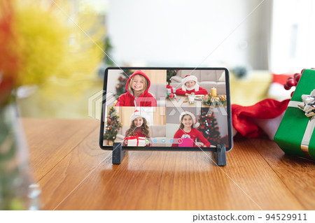 Four smiling caucasian girls in santa hats on tablet christmas group video call interface screen Four smiling caucasian girls in santa hats on tablet christmas group video call interface screen 94529911