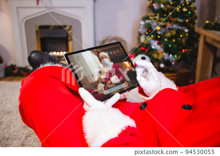 Santa claus making tablet christmas video call with man in santa costume wearing face mask Santa claus making tablet christmas video call with man in santa costume wearing face mask 94530055