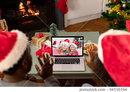 Waving african american couple making laptop christmas video call with smiling mother and daughter 94530394