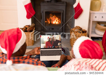 African american couple making laptop christmas video call with smiling caucasian couple 94530444