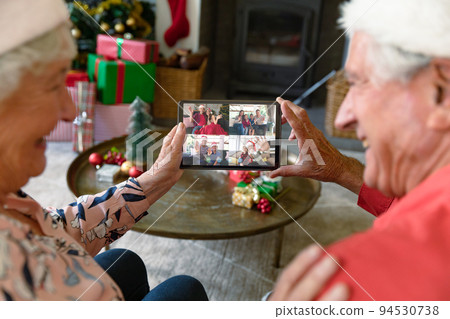 Caucasian senior couple in santa hats on christmas video call on tablet with friends and family 94530738