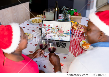 African american senior couple in santa hat with vine on christmas laptop video call with family 94530765