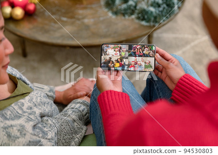 Two diverse female friends on christmas video call on smartphone with family Two diverse female friends on christmas video call on smartphone with family 94530803