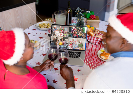 African american senior couple in santa hat with vine on christmas laptop video call with family 94530810