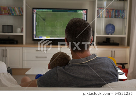 Caucasian father with son watching tv with football match on screen Caucasian father with son watching tv with football match on screen 94531285