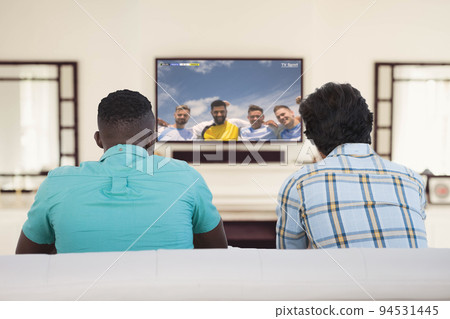 Two diverse friends sitting on the couch and watching football match Two diverse friends sitting on the couch and watching football match 94531445