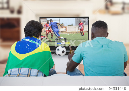 Two diverse friends sitting on the couch and watching football match 94531448