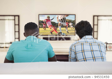 Two diverse friends sitting on the couch and watching football match Two diverse friends sitting on the couch and watching football match 94531450