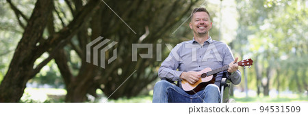 Male street musician plays guitar in wheelchair 94531509
