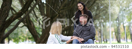 Two women and man in a wheelchair are talking in park 94531510