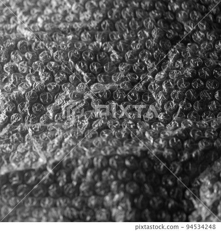 Reflecting light and shadow on creases and tears in plastic bubble wrap sheeting on black 94534248