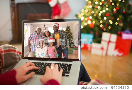 Caucasian woman on laptop christmas video call with smiling friends in santa hats 94534350